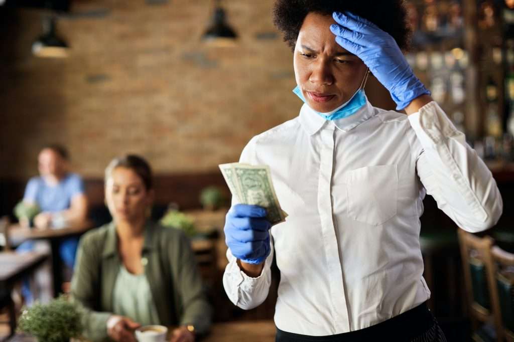 African American waitress feeling dissatisfied with a tip from a customer in a cafe.