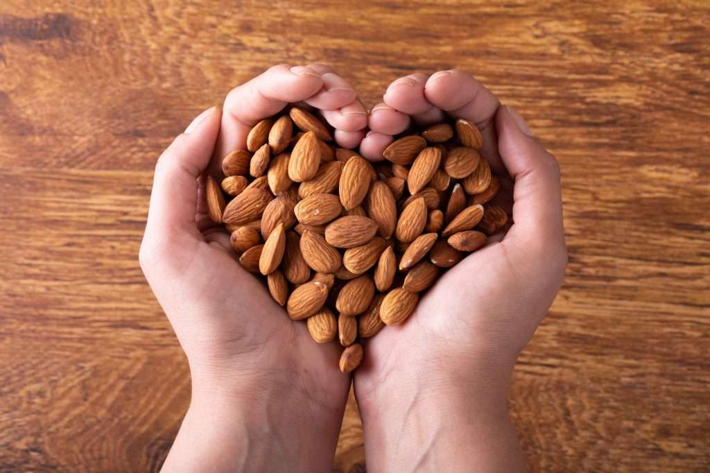 Cropped hands holding nutritious almonds in heart shape on wooden table