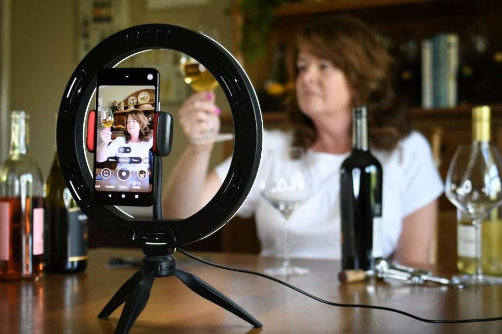 Female leading virtual wine tasting online video social media or live stream with light ring & phone