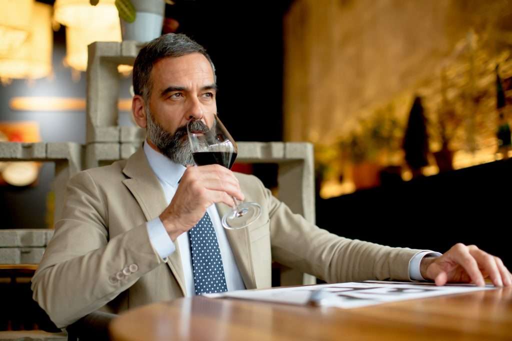 Handsome bearded businessman drinking red wine in restaurant