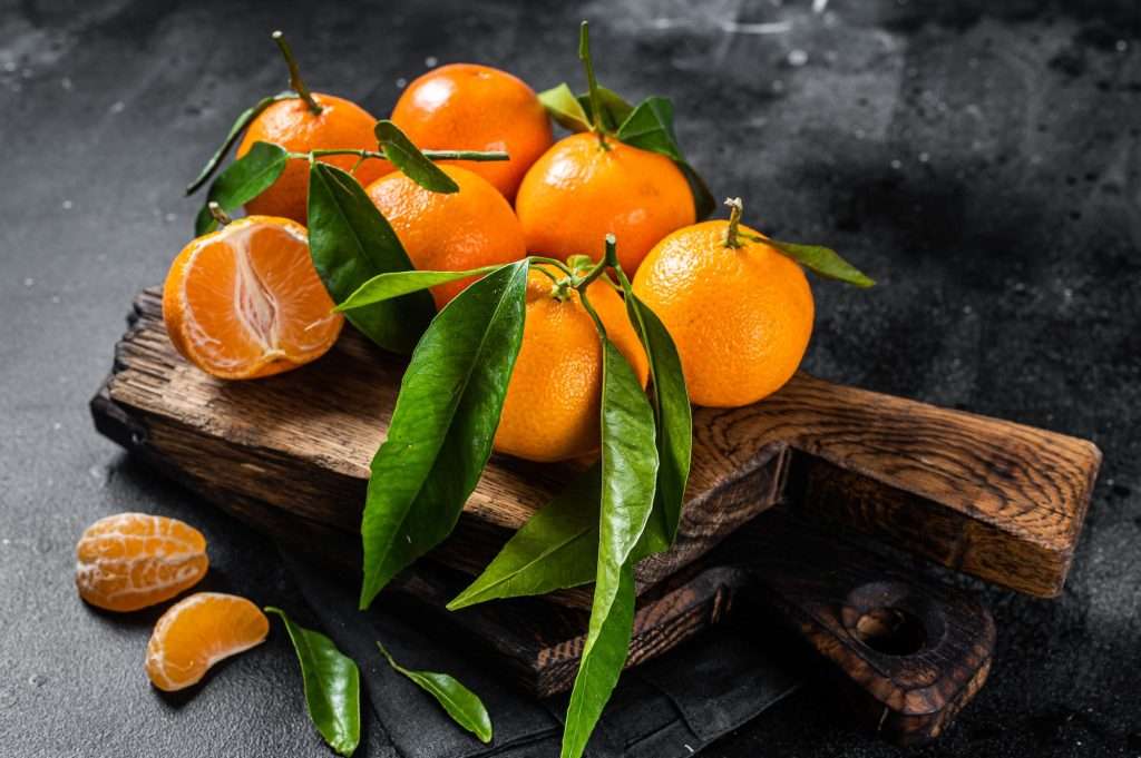 Mandarin oranges or tangerines fruits with leaves on wooden board. Black background. Top view