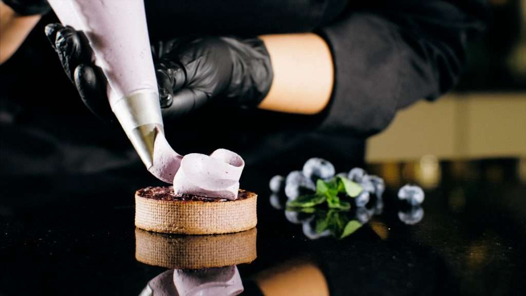 Pastry chef decorates biscuit with purple cream from pastry bag, close-up
