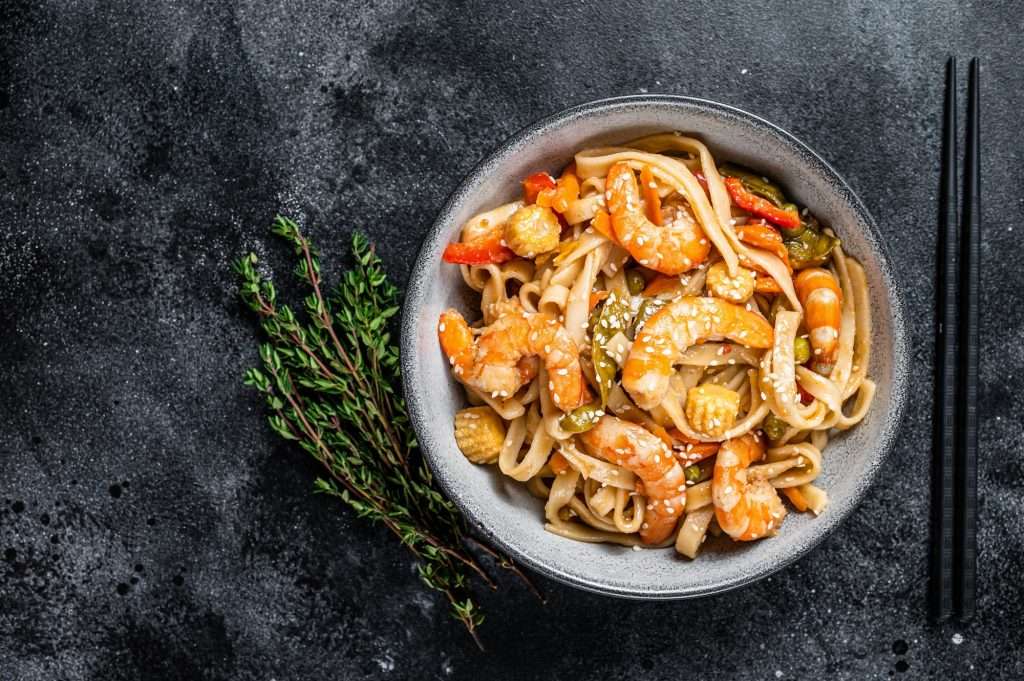 Stir-fry udon seafood noodles with shrimp prawns in a bowl. Black background. Top view. Copy space
