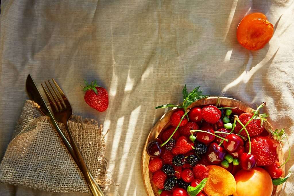 Summer fruits and berries seasonal background with cutlery under natural light