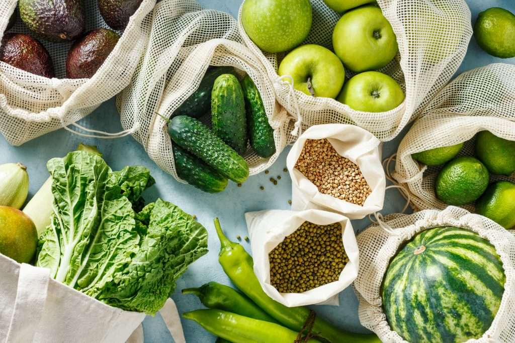 Various green vegetables, fruits and grains in reusable bags. Top view