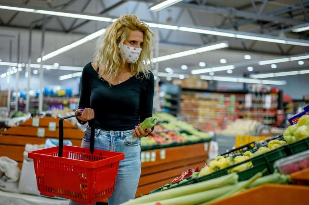 Woman in a supermarket jumping and wearing protective face mask while grocery shopping