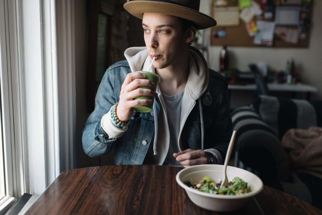 Young man sitting at table, having meal, drinking health drink